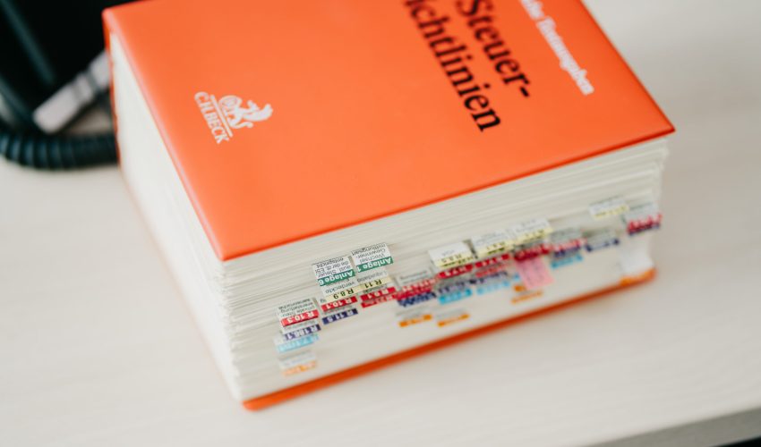 dickes fachbuch steuerrichtlinien mit zahlreichen markierungen auf schreibtisch